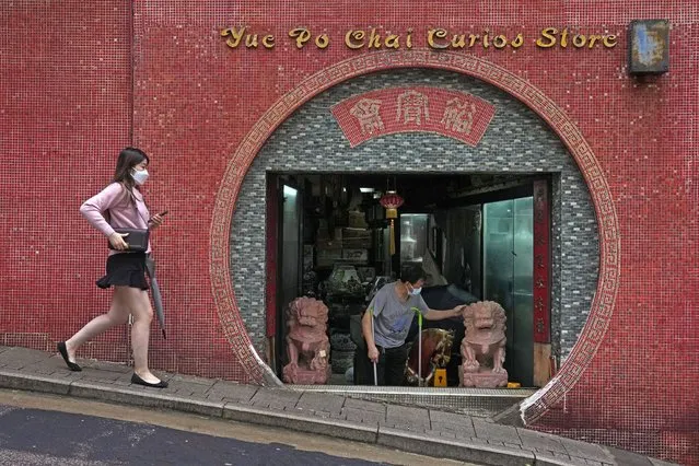 A woman wearing a mask walks past an antique store in Hong Kong, Friday, March 25, 2022. (Photo by Kin Cheung/AP Photo)