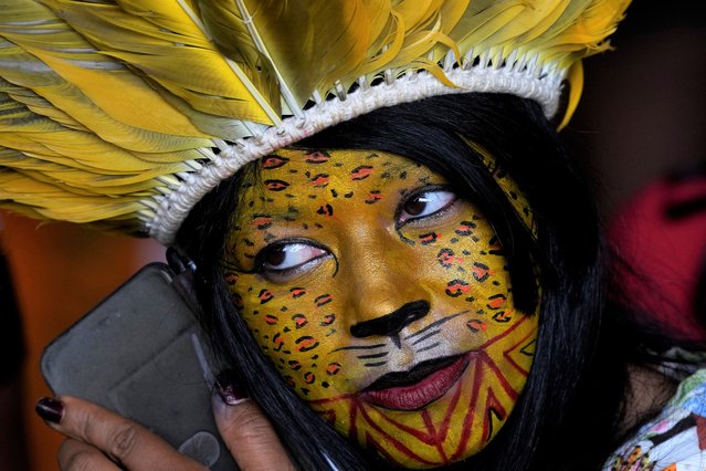A Pataxo woman listens to her cell phone as she waits for the start of the Indigenous people's meeting with Brazil's former President Luiz Inacio Lula da Silva, as part of the 18th annual Free Land Indigenous Camp, in Brasilia, Brazil, Tuesday, April 12, 2022. (Photo by Eraldo Peres/AP Photo)