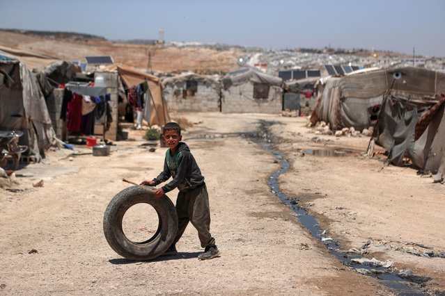 A Syrian boy plays with a tire near sewage canals that run between the tents at a camp for internally displaced people (IDP) near Sarmada, in the northern Syrian province Idlib on June 28, 2024. After 13 years of civil conflict, lack of international funding has severely undercut the provision of basic services such as water, waste disposal and sanitation in displacement camps in northwest Syria, according to the United Nations. More than five million people, most of them displaced, live in areas outside government control in Syria's north and northwest, according to the UN, many relying on aid to survive. (Photo by Aaref Watad/AFP Photo)