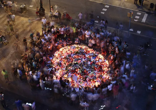 People gather at a memorial tribute of flowers, messages and candles to the victims on Barcelona's historic Las Ramblas promenade on the Joan Miro mosaic, embedded in the pavement where the van stopped after killing at least 13 people in Barcelona , Spain, Friday, August 18, 2017. (Photo by Manu Fernandez/AP Photo)