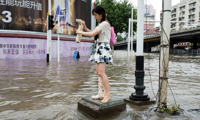 This picture taken on July 6, 2016 shows a woman emptying the water from her boots at a flooded area in Wuhan, central China's Hubei province. Heavy rain around China's Yangtze river basin has left 128 people dead and scores missing, media said on July 5, with more damage feared from a typhoon expected to land this week. (Photo by AFP Photo/Stringer)