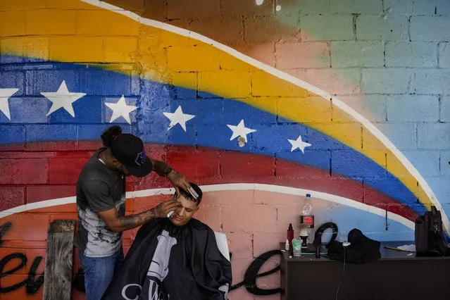 A barber cuts a client's hair at his shop in the San Agustin neighborhood of Caracas, Venezuela, Sunday, July 17, 2022. (Photo by Matias Delacroix/AP Photo)