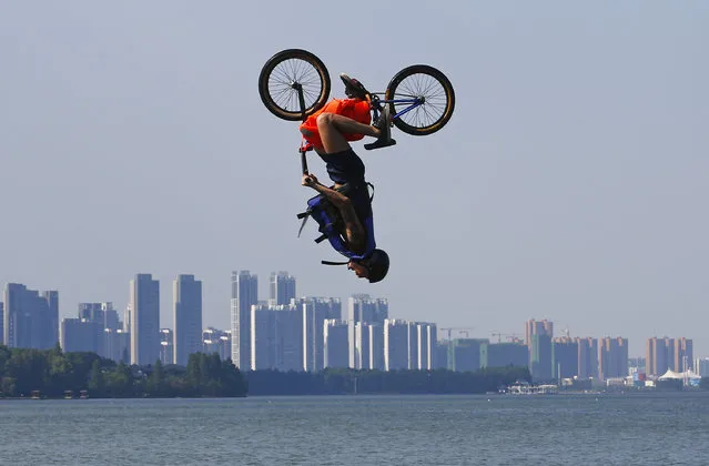 An extreme cycling enthusiast performs a stunt with a bicycle before falling into the East Lake in on July 24, 2016 in Wuhan, Hubei province, China. This activity, which requires participants to ride their bikes and jump into the lake, attracts many extreme cycling enthusiasts from the city. (Photo by Wang He/Getty Images)