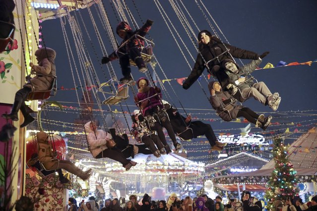Children and their parents ride a carousel at a Christmas Market set up in Red Square decorated for the New Year and Christmas festivities in Moscow, Russia, Sunday, December 31, 2023. The Red Square will be closed for celebrations on the New Year's Eve. (Photo by Marina Lystseva/AP Photo)
