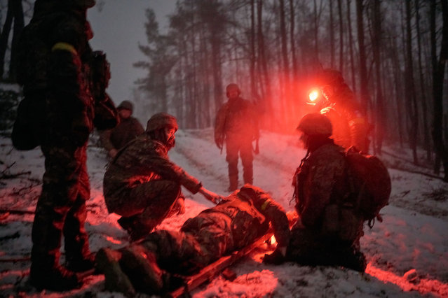 Medics evacuate a wounded soldier who tripped on a petal mine as evacuation takes place in darkness in the middle of a damaged forest on January 27, 2024 in Kupiansk Frontline, Ukraine. The Edelweiss Brigade (also spelled Edelveys), a specialized unit within the Ukrainian ground forces, is trying to fend off near-constant Russian attacks on Kupiansk, which is mere kilometers from the frontline. Ukrainian soldiers, mountain assault infantry, hold the front in the winter forest. (Photo by Kostiantyn Liberov/Libkos/Getty Images)