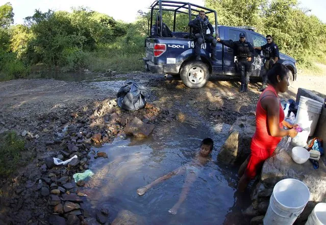 A woman washes clothes (R) as a boy sits in a small river next to federal police officers standing guard along a road, at an area near clandestine graves in Pueblo Viejo, on the outskirts of Iguala in the southern Mexican state of Guerrero October 11, 2014. (Photo by Jorge Dan Lopez/Reuters)