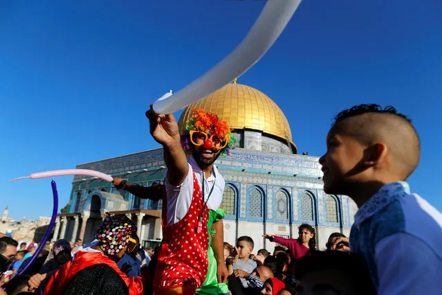 A man dressed as clown entertains children following morning prayers marking the first day of Eid al-Adha celebrations, on the compound known to Muslims as al-Haram al-Sharif and to Jews as Temple Mount in Jerusalem's Old City September 12, 2016. The Dome of the Rock is seen in the background. (Photo by Ammar Awad/Reuters)