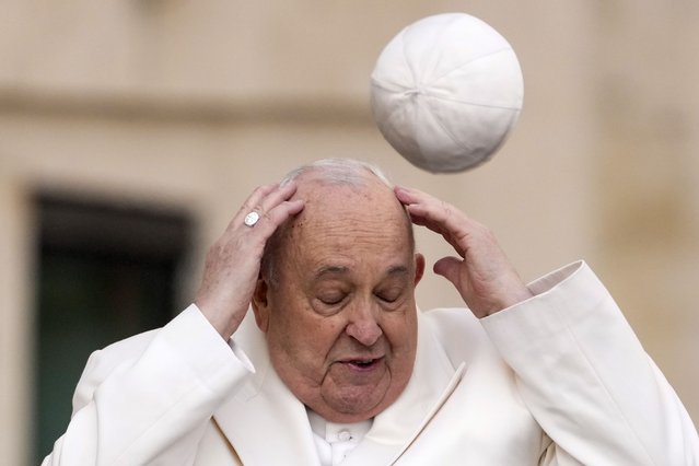 Pope Francis tries to catch his cap as wind blew it away while arriving for his weekly general audience in the St. Peter's Square at the Vatican, Wednesday, March 13, 2024. (Photo by Andrew Medichini/AP Photo)