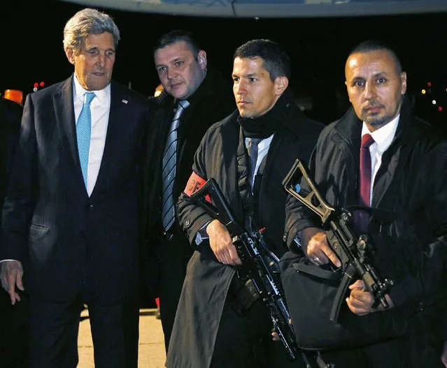 US Secretary of State John Kerry (L) looks over the weapons carried by Swiss police posing for a picture with him as he departs Geneva late on January 14, 2015. Top diplomats from Iran and the United States held “substantive” talks on January 14 aimed at speeding up negotiations for a nuclear deal, with US Secretary of State John Kerry heading back for a surprise new round. (Photo by Rick Wilking/AFP Photo)