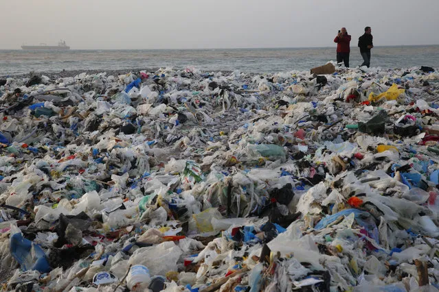 In this Monday, January 22, 2018, photo, a man takes photos of piles of garbage washed on shore after an extended storm battered the Mediterranean country at the Zouq Mosbeh costal town, north of Beirut, Lebanon. Environmentalists say a winter storm has pushed a wave of trash onto the Lebanese shore outside Beirut, stirring outrage over a waste management crisis that has choked the country since 2015. (Photo by Hussein Malla/AP Photo)