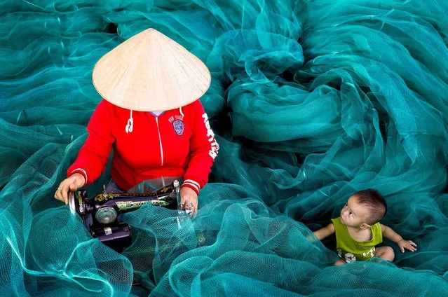 Traditional seamstresses meticulously examine amoungst a sea of bright blue fishing nets before having a nap on the job in Phan Rang, central Vietnam in November 2022. (Photo by Hilton Chen/Solent News & Photo Agenc)