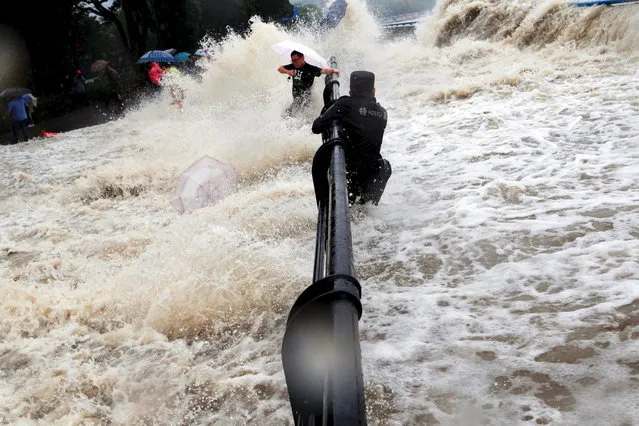 A paramilitary policeman holds onto a fence as tourists dodge tidal waves increased under the influence of Typhoon Dujuan, in Hangzhou, China, September 2015. (Photo by Reuters/Stringer)