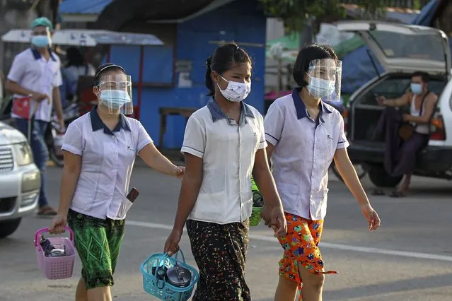 Factory workers wearing protective face masks and shields cross a road as they go to work in Hlaing Tharyar Industrial Zone Monday, October 12, 2020, on the outskirts of Yangon, Myanmar. Myanmar government allowed Monday to resume Cut-Make-Pack (CMP) factories, workplaces and SMEs that meet “A-level” practices in COVID-19 containment measures by authorities even though higher numbers of positive cases found daily. Myanmar reached over 20,000 confirmed cases and more than 600 death with COVID-19. (Photo by Thein Zaw/AP Photo)