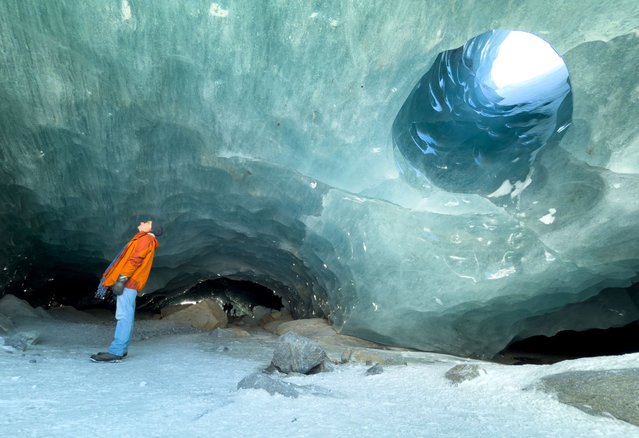 A man looks inside in one of the ice caves formed by water during the summer on the tongue the Morteratsch glacier as it melts due to climate change in Pontresina near Saint Moritz in eastern Switzerland, on February 21, 2025. (Photo by Denis Balibouse/Reuters)