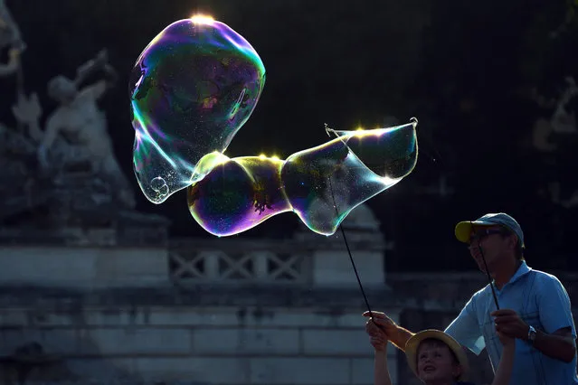 A street seller teaches a boy how to make soap bubbles, on Piazza del Popolo, a touristic square in central Rome at sunset on July 2, 2015. (Photo by Gabriel Bouys/AFP Photo)