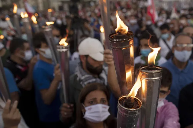 Anti-government protesters hold up torches as they lit a giant flame over a metal statue that reads in Arabic: “October 17, Revolution”. next to the site of the Aug. 4 deadly blast in the seaport of Beirut that killed scores and wounded thousands in Beirut, Lebanon, Saturday, October 17, 2020. Thousands of people marked the first anniversary of the protest movement in different parts of Lebanon including the three largest cities, Beirut, Tripoli and Sidon. (Photo by Hassan Ammar/AP Photo)