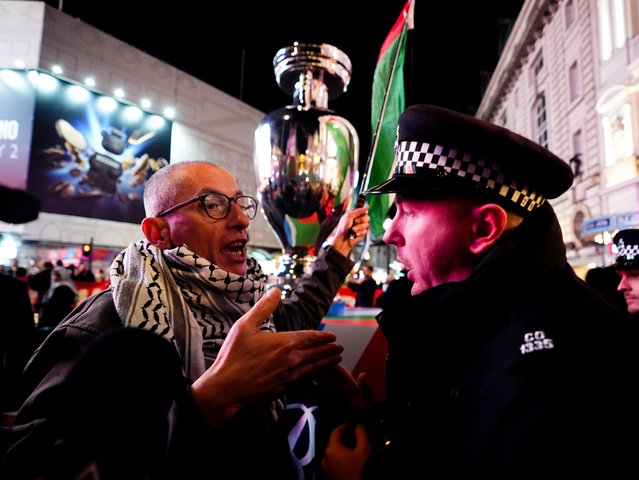 A protester speaking with a police officer near a replica UEFA trophy, Piccadilly Circus, London on Wednesday, November 12, 2025, following the UEFA EURO 2028 launch at Below The Lights. The tournament was officially launched at an event in central London on Wednesday, which included an unveiling of the match schedule. (Photo by James Manning/PA Wire)