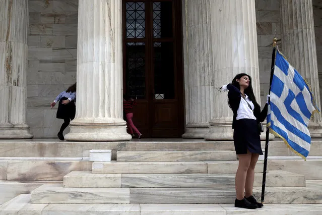 Children (L) play hide and seek as a student holds a Greek national flag at the entrance of the Athens Academy, following a student parade marking the “Ohi” (No) day, the country's rejection on Italy's ultimatum to surrender as the World War II flared up, in Athens, Greece, October 28, 2016. (Photo by Alkis Konstantinidis/Reuters)