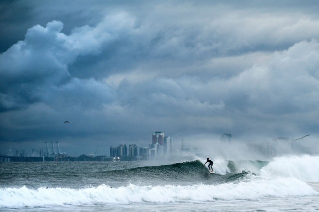 A surfer rides a wave as clouds gather above the Bolsa Chica State Beach in Orange County, California, on Saturday, November 15, 2025. (Photo by Noah Berger/AP Photo)
