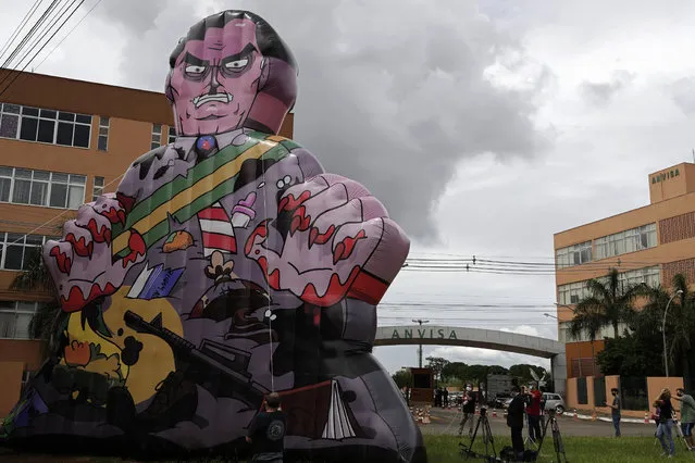 Demonstrators raise large puppet representing Brazil's President Jair Bolsonaro as a killer in front of  Brazil's health agency, before agency directors meet to assess the emergency use of China's Sinovac Biotech and the Oxford/AstraZeneca COVID-19 vaccines, at the Anvisa agency's headquarters in Brasilia, Brazil, Sunday, January 17, 2021. (Photo by Eraldo Peres/AP Photo)