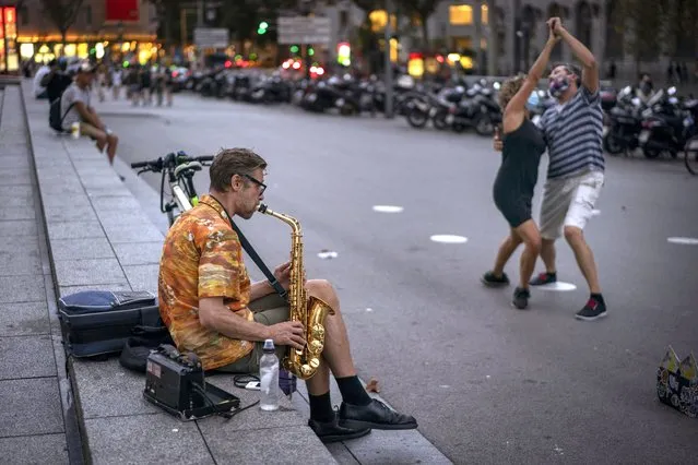 A man plays his saxophone as a couple wearing face masks dance in the street in Barcelona, Spain on Friday, August 28, 2020. Spanish authorities have announced new restrictions to prevent COVID-19. (Photo by Emilio Morenatti/AP Photo)