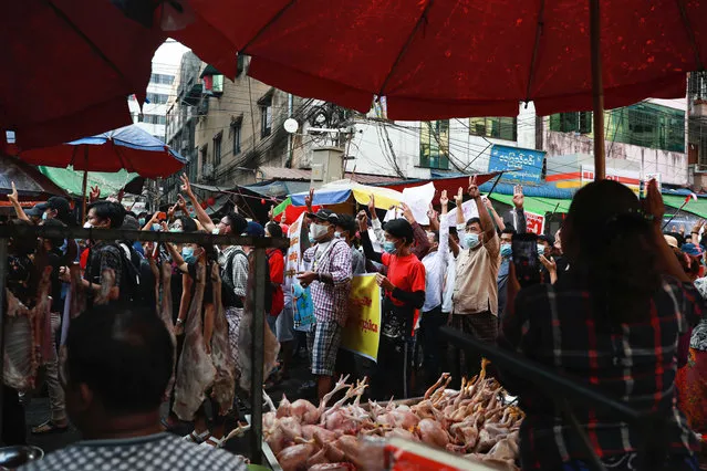 Protester flash the three-fingered salute as they march past meat vendors in Yangon, Myanmar on Sunday, Feb. 7, 2021. Thousands of people rallied against the military takeover in Myanmar's biggest city on Sunday and demanded the release of Aung San Suu Kyi, whose elected government was toppled by the army that also imposed an internet blackout. (Photo by AP Photo/Stringer)