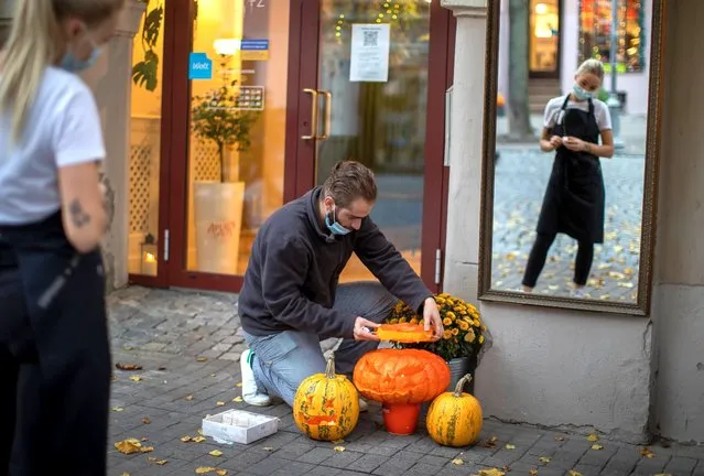 A restaurant employee wearing a mask for protection against the COVID-19 infection, decorates the entrance to a restaurant at the Old Town in Vilnius Lithuania, Friday, October 30, 2020. Given the deteriorating epidemiological situation in the country, the Government has taken a decision in its Wednesday sitting to impose restrictions on events and gatherings organised in public places from 30 October to 13 November 2020. (Photo by Mindaugas Kulbis/AP Photo)