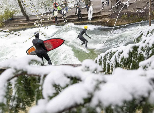 Surfers stand in icy temperatures and snow with their boards at the Eisbach in the English Garden, which is located in the heart of the Bavarian capital in Munich, Germany, Saturday, April 2, 2022. The Eisbach wave is a real hotspot at any time of year. (Photo by Peter Kneffel/dpa via AP Photo)