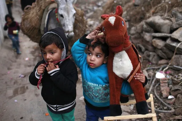 A young boy carries his rocking horse toy on his shoulder next to another boy in an ally inside a Christian colony in Islamabad January 20, 2015. (Photo by Sara Farid/Reuters)