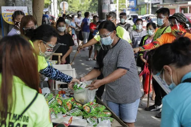 A woman receives free food at a makeshift stall called “Community Pantry” beside a road in Quezon city, Philippines on Monday, April 19, 2021. Donated food and other essential items from residents or volunteers are placed on makeshift stalls for people who need it as many have lost jobs due to quarantine measures set by the government to curb the surge in COVID-19 cases in the country. The “Community Pantry” which started in Maginhawa street has spread to several areas around the metropolitan to support people struggling to make ends meet. (Photo by Aaron Favila/AP Photo)