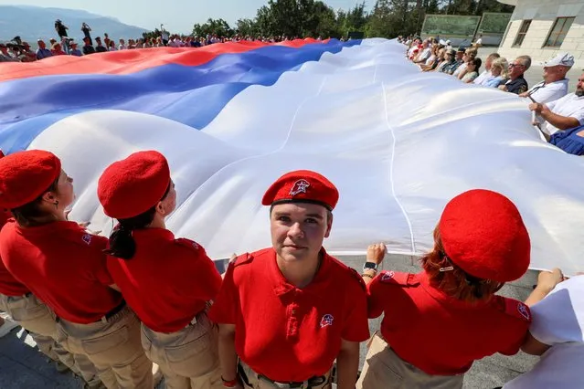 Participants, including members of Russia's Youth Army military-patriotic movement, gather around a large-size Russian state flag during an event marking National Flag Day in the Black Sea port of Sevastopol, Crimea on August 22, 2023. (Photo by Alexey Pavlishak/Reuters)