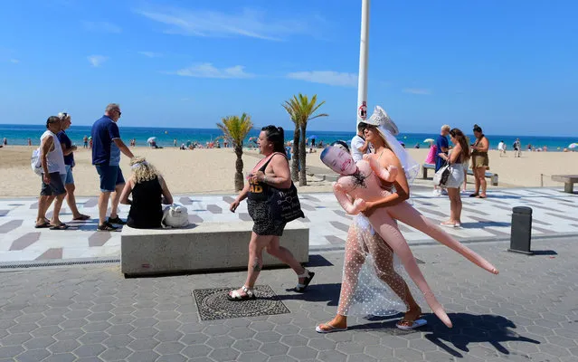 A woman carries an inflatable dummy as she walks along the promenade at Levante Beach in Benidorm on June 7, 2022. Whether it's chefs, bar staff or dishwashers, many bars, restaurants and cafes across Benidorm are struggling to recruit workers, generating a new source of tension after two years of pandemic. (Photo by Jose Jordan/AFP Photo)
