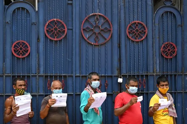 Workers hold documents as they wait for their turn to receive the first dose of Covishield vaccine against the Covid-19 coronavirus in a passenger bus converted into a mobile vaccination centre at a wholesale market in Kolkata on June 3, 2021. (Photo by Dibyangshu Sarkar/AFP Photo)