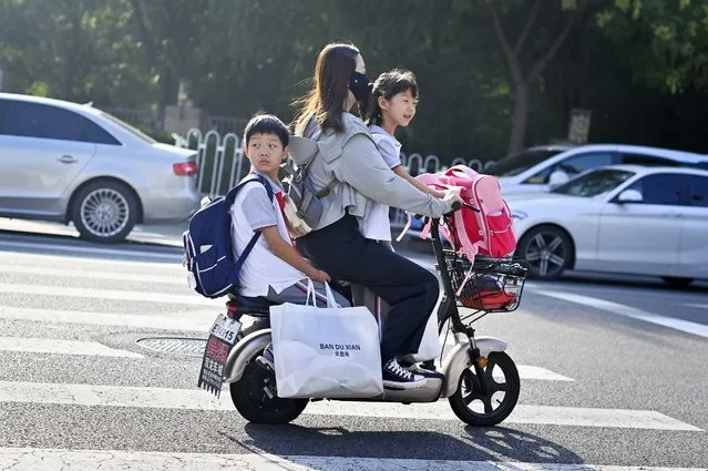 A woman rides her electric scooter with two primary school-aged chilren as they head for classes on the first day of the new semester in Beijing on September 1, 2023. (Photo by Wang Zhao/AFP Photo)
