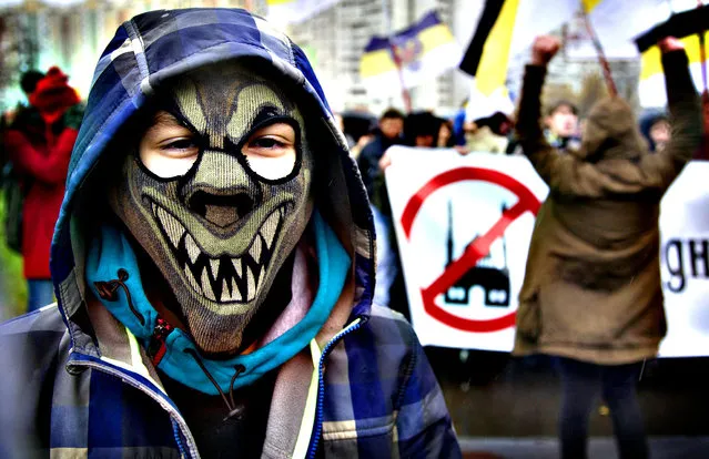 Nationalist demonstrator wears a masks as others carry a banner reading “Today a Mosque – tomorrow Jihad” at left, during a march to mark National Unity Day, in Moscow, Russia, on Monday, November 4, 2013. Several thousand Russian nationalists rallied Monday in Moscow, venting against the migrants they accuse of pushing up the crime rate and taking their jobs. The protest took place on the national holiday of Unity Day, established in 2005 to replace commemorations of the Bolshevik Revolution. (Photo by Ivan Sekretarev/AP Photo)