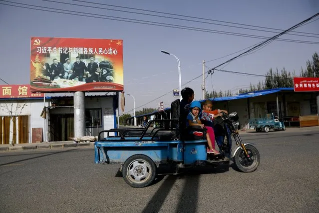 In this September 20, 2018, file photo, an Uighur woman shuttles school children on an electric scooter as they ride past a propaganda poster showing China's President Xi Jinping joining hands with a group of Uighur elders in Hotan, in western China's Xinjiang region. Under Chinese President Xi Jinping, the Uighur homeland has been blanketed with stifling surveillance, from armed checkpoints on street corners to facial-recognition-equipped CCTV cameras steadily surveying passers-by. Now, Uighurs say, they must live under the watchful eye of the ruling Communist Party even inside their own homes. (Photo by Ng Han Guan/AP Photo)