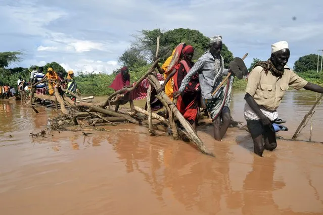 Residents of Chamwana Muma village walk through flood water after using a makeshift bridge to cross the swollen River Tana, in Tana Delta, Kenya, on Wednesday November 15, 2023. Unrelenting rainfall across Kenya's northern counties and the capital, Nairobi, has led to widespread flooding, displacing an estimated 36,000 people and killing 46 people since the beginning of the rainy season less than a month ago. (Photo by Gideon Maundu/AP Photo)