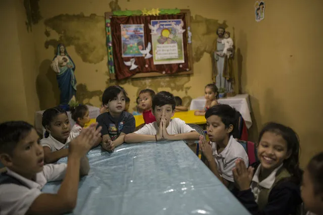 Children pray before lunch in San Antonio de Padua popular dinning room in Petare slum, Caracas, Venezuela, Monday, February 11, 2019. (Photo by Rodrigo Abd/AP Photo)
