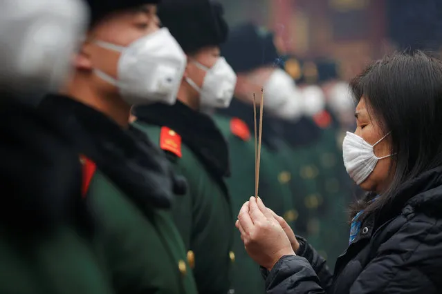 A woman holding incense sticks and paramilitary policemen wear face masks as people gather at Yonghegong Lama Temple to pray for good fortune on the first day of the Lunar New Year of the Rooster in Beijing, China January 28, 2017. (Photo by Damir Sagolj/Reuters)