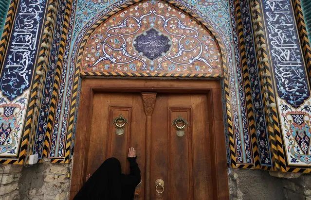 A Shiite pilgrim touches the door of the shrine of 8th-century Imam Musa al-Kadhim to commemorate his death in the Kadhimiya district north of Baghdad on February 5, 2024. Pilgrims from various Iraqi provinces undertake a march on foot to reach the shrine in the capital to commemorate the 795 CE death of Imam Musa, who is believed to have been poisoned by agents of the then ruler Harun al-Rashid. (Photo by Ahmad Al-Rubaye/AFP Photo)