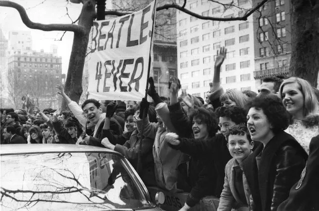 Screaming teenagers, mostly girls, wave a banner “Beatles forever” welcoming the British band from Liverpool, The Beatles, outside the Plaza Hotel in New York City, USA, February 7, 1964. The band will appear on television and will give two concerts at Carnegie Hall. (Photo by AP Photo)