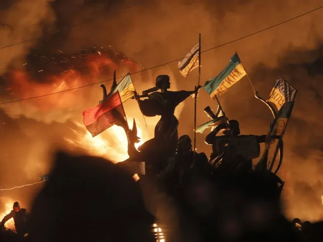 Monuments to Kiev's founders burn as anti-government protesters clash with riot police in Kiev's Independence Square, the epicenter of the country's current unrest, Kiev, Ukraine, Tuesday, February 18, 2014. Thousands of police armed with stun grenades and water cannons attacked the large opposition camp in Ukraine's capital on Tuesday that has been the center of nearly three months of anti-government protests after at least nine people were killed in street clashes. (Photo by Efrem Lukatsky/AP Photo)