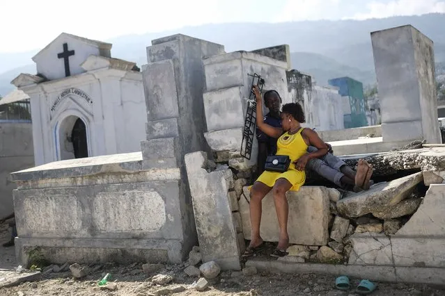 People sit on a tomb at the National Cemetery on the Fete Gede celebration of spirits holiday in Port-au-Prince, Haiti, Monday, November 1 2021. The celebration of the spirits is equivalent to the Roman Catholic festivity of the Day of the Dead and All Saints Day. (Photo by Matias Delacroix/AP Photo)