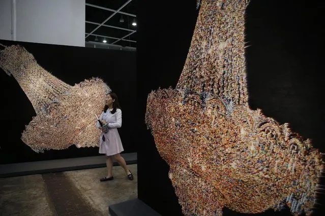 A woman walks past an artwork “Chandeliers for Five Cities” created by South Korean artist Ham Kyungah during the VIP preview of the art fair “Art Basel” in Hong Kong, Tuesday, March 22, 2016. Ham presented “Chandeliers in Five Cities”, the latest in her series of embroidered works crafted with the help of unidentified North Korean workers. Ham settled on chandeliers as a reference to political power after she noticed one in a picture of world leaders meeting to divide the Korean Peninsula into north and south at the end of World War II. (Photo by Kin Cheung/AP Photo)