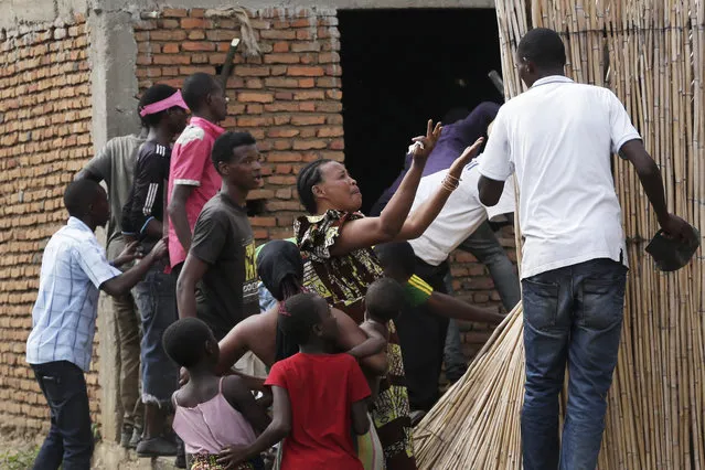 A crying woman argues with demonstrators who cornered a suspected member of the ruling party's Imbonerakure youth militia at his home in the Cibitoke district of Bujumbura, Burundi, Thursday May 7, 2015. Jean Claude Niyonzima, a suspected member of the ruling party's Imbonerakure youth militia, fled from his house into a sewer under a hail of stones thrown by a mob protesting against President Pierre Nkurunziza's decision to seek a third term in office. (Photo by Jerome Delay/AP Photo)