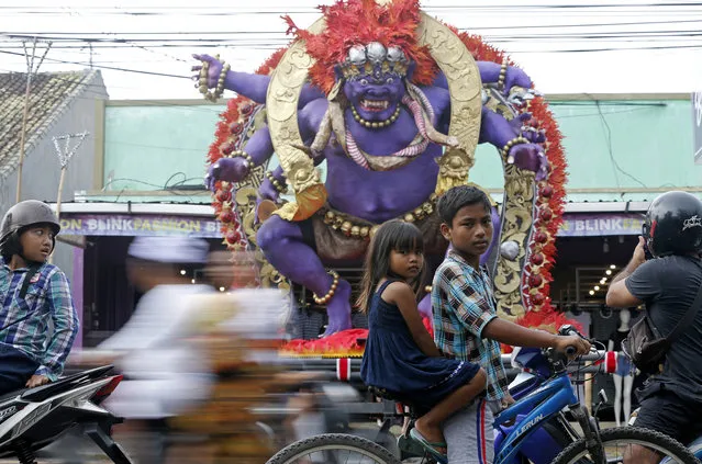 Children on their bicycle move past a giant effigy locally known as “ogoh-ogoh” that represents evil spirits to celebrate Nyepi, the annual day of silence marking Balinese Hindu new year in Bali, Indonesia, Wednesday, March 6, 2019. Most Balinese practice self-reflection and stay at home to observe the quiet holiday, and tourists visiting the island are asked not to leave their hotels and the airport will be closed. (Photo by Firdia Lisnawati/AP Photo)
