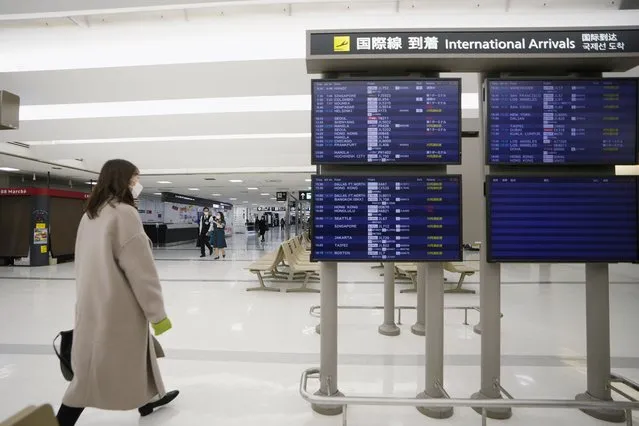 A passenger walks by arrival information screens for international flights at the Narita International Airport in Narita, east of Tokyo, Thursday, December 2, 2021. Going further than many other countries in trying to contain the virus, Japan has banned foreign visitors and asked international airlines to stop taking new reservations for all flights arriving in the country until the end of December. (Photo by Hiro Komae/AP Photo)