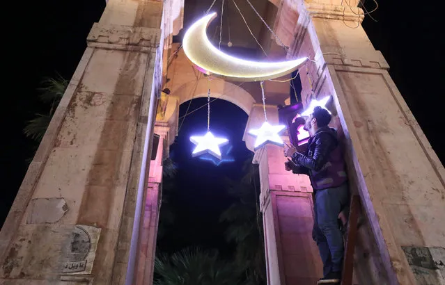 A Syrian man adjusts decorations for the Muslim holy fasting month of Ramadan at the Clock Square in Syria's rebel-held northwestern city of Idlib, on April 12, 2021. (Photo by Omar Haj Kadour/AFP Photo)