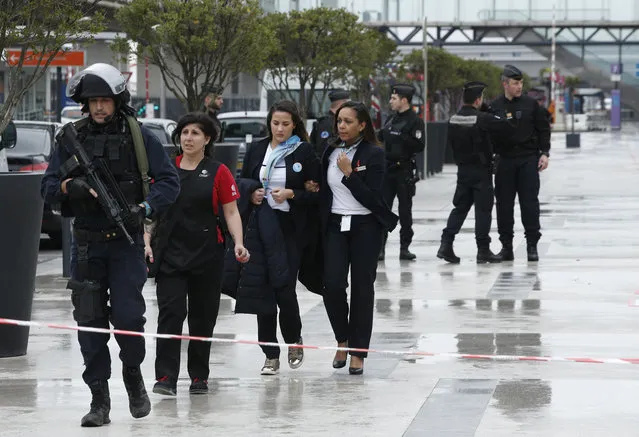 A police officer escorts airport employees outside the Orly airport , south of Paris, Saturday, March, 18, 2017. A man was shot dead after wrestling a soldier to the ground at Paris' Orly Airport and trying to take her rifle, officials said. No one else in the busy terminal was hurt, but thousands of travelers were evacuated and flights were diverted to the city's other airport. (Photo by Thibault Camus/AP Photo)