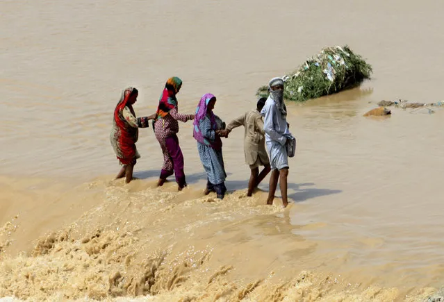 Pakistani family members help each others to cross stream caused by heavy rainfall in Karachi, Pakistan, Wednesday, July 31, 2019. Every year, many cities in Pakistan struggle to cope with the annual monsoon deluge, drawing criticism about poor planning. The monsoon season runs from July through September. (Photo by Fareed Khan/AP Photo)